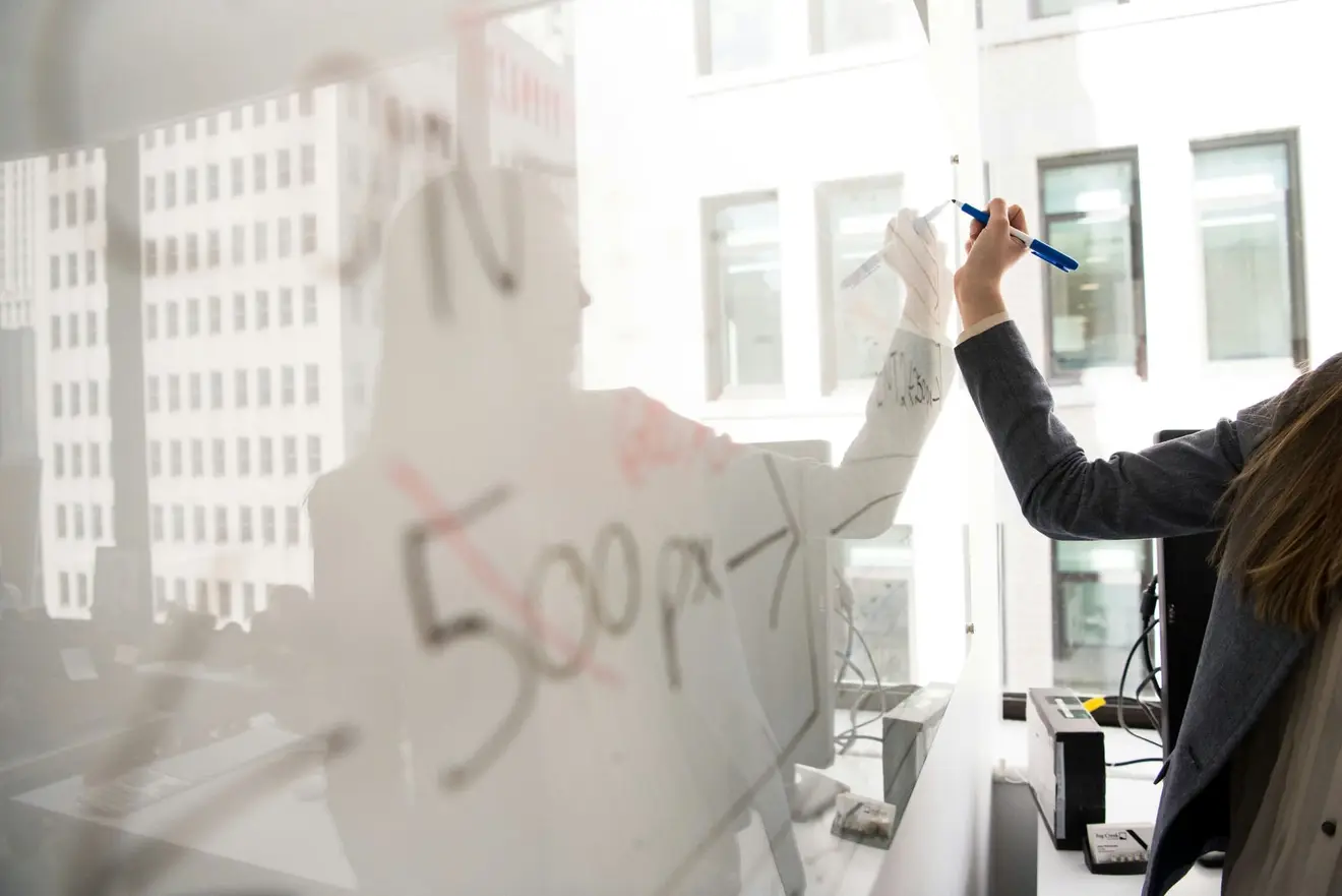 A woman in a grey blazer working through a plan in marker on a glass office wall, the building across the street reflected in the pane: with South Africa out of the equation, the destination country's own dual-nationality rule is the variable you now map at the visa-choice stage
