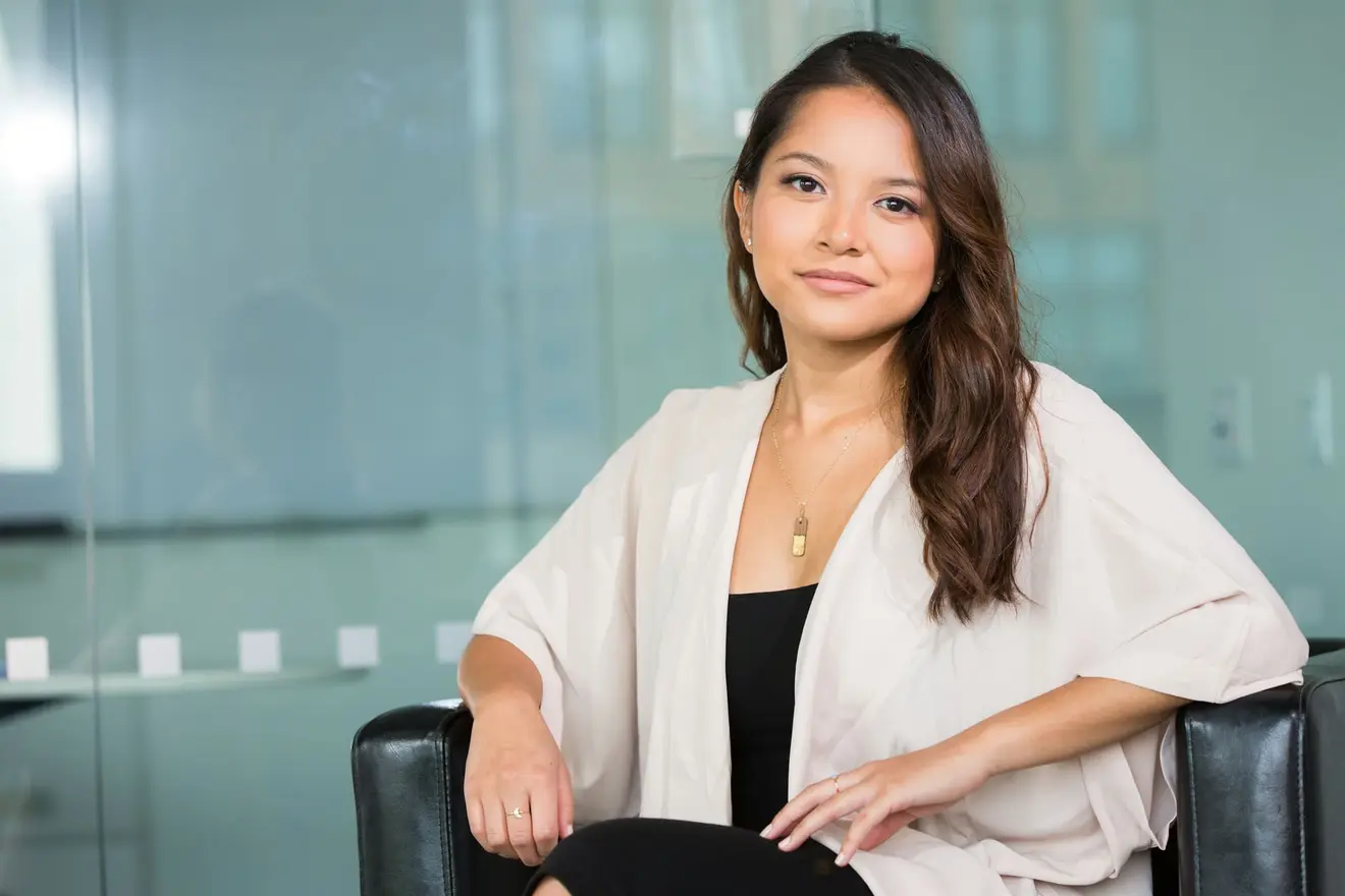 A founder seated in a black leather armchair against a glass office wall, one arm resting along the back of the chair, looking straight at the camera, the settled posture of someone who has already worked through the five questions below