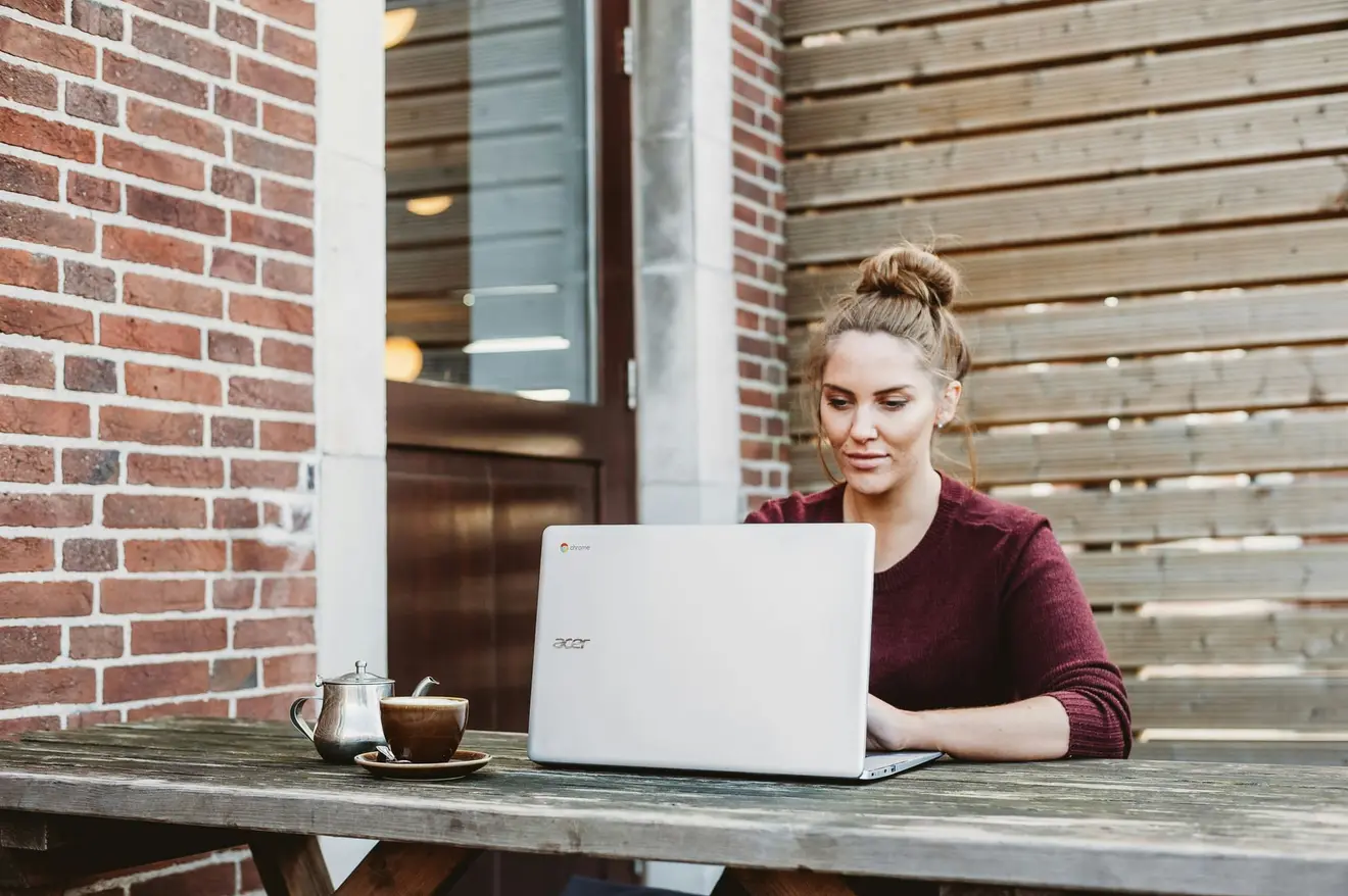 A founder working alone at an outdoor cafe table with a laptop and a coffee, the kind of admin session that produces the bank statements and source-of-funds trail a Spanish consulate expects
